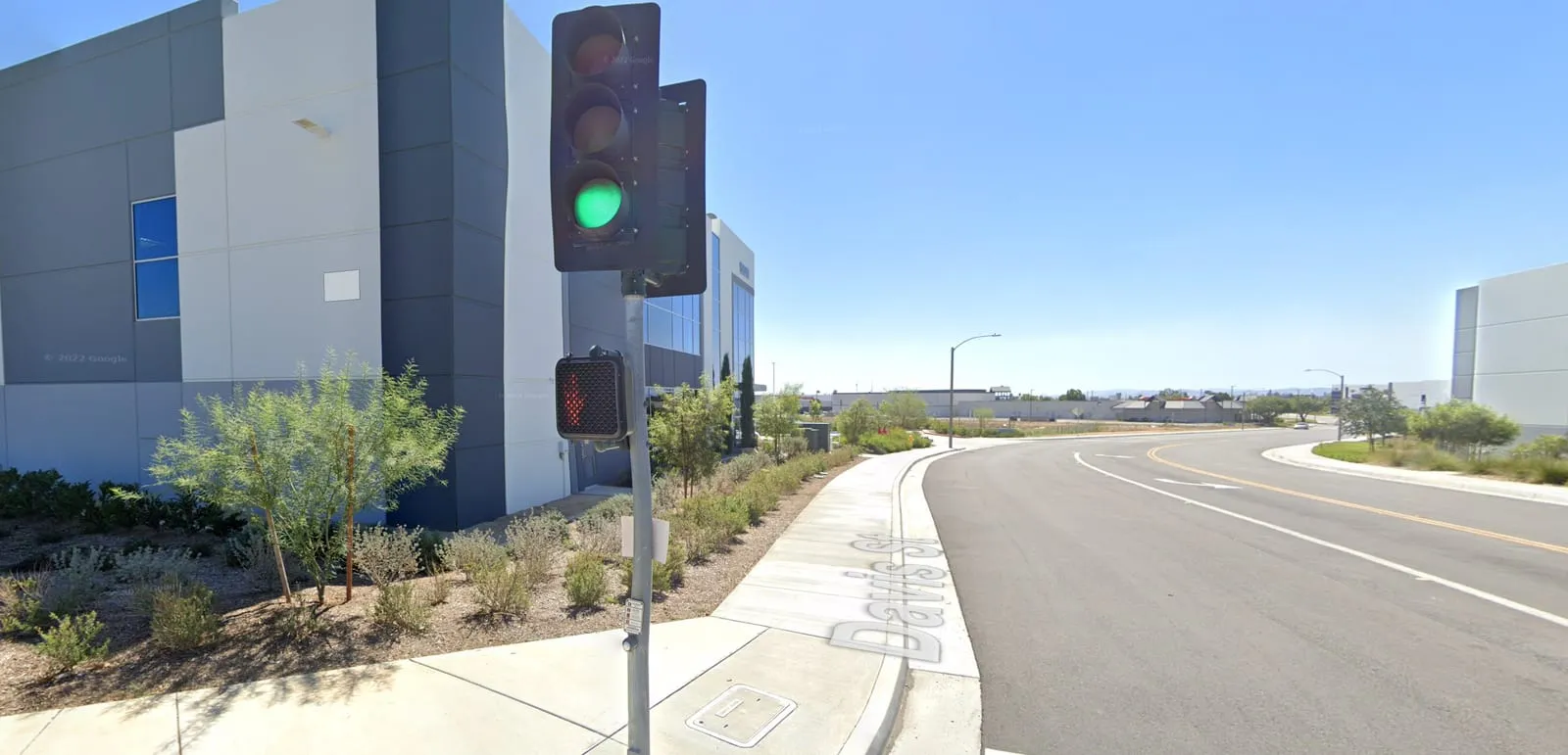 New warehouse buildings along a wide, empty road with landscaped sidewalks and a traffic signal.